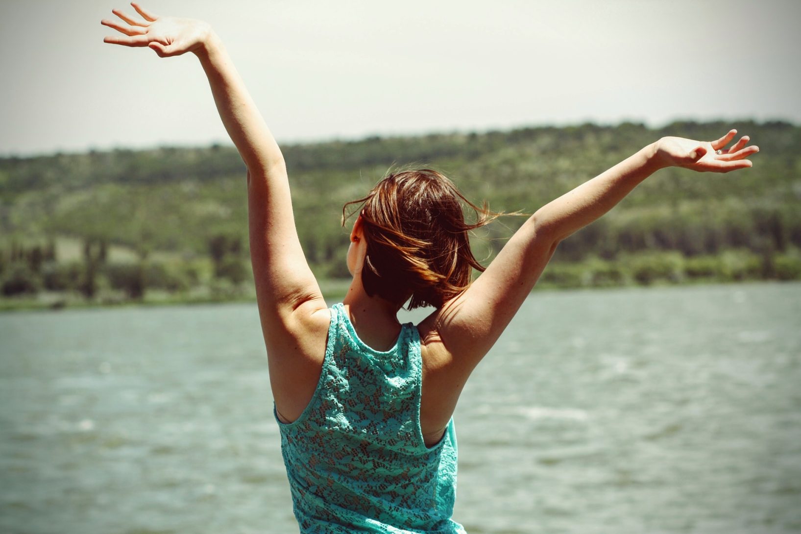 Woman looking out at lake with arms above head featured on page about Naturopathic Care for Complex Chronic Illness in Oregon